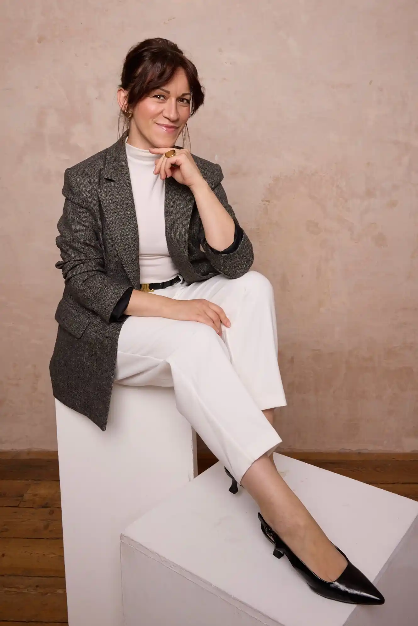 Agata Prywer assise sur un cube blanc, en veste grise et pantalon blanc